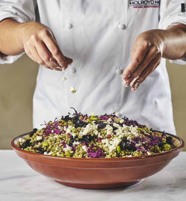 Careers. A chef in a white coat sprinkles crumbled cheese over a colourful salad with greens and purple cabbage.