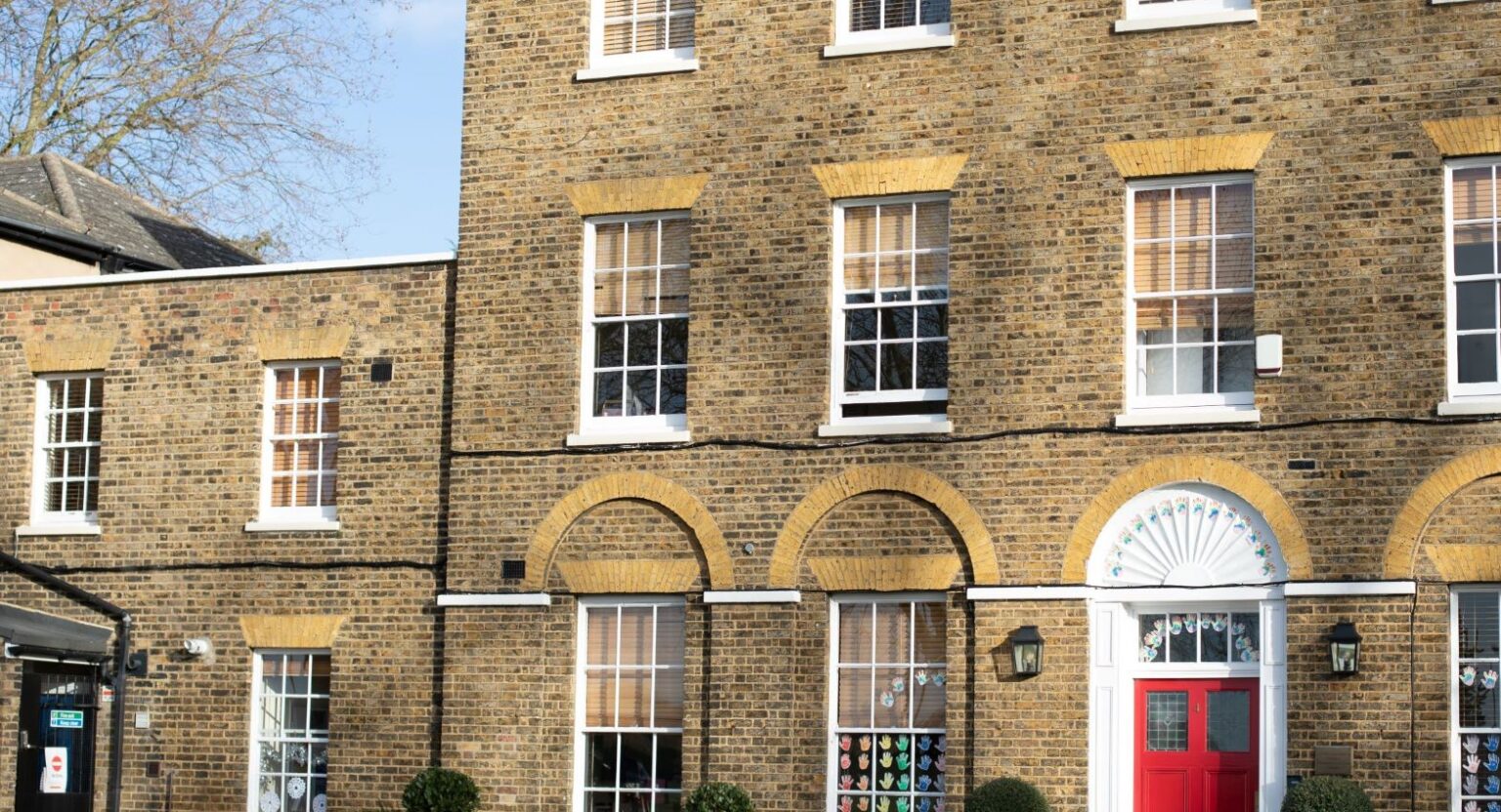 A picture of Blackheath Prep School; A three-story brick building with a red door, white trim, and multiple windows.