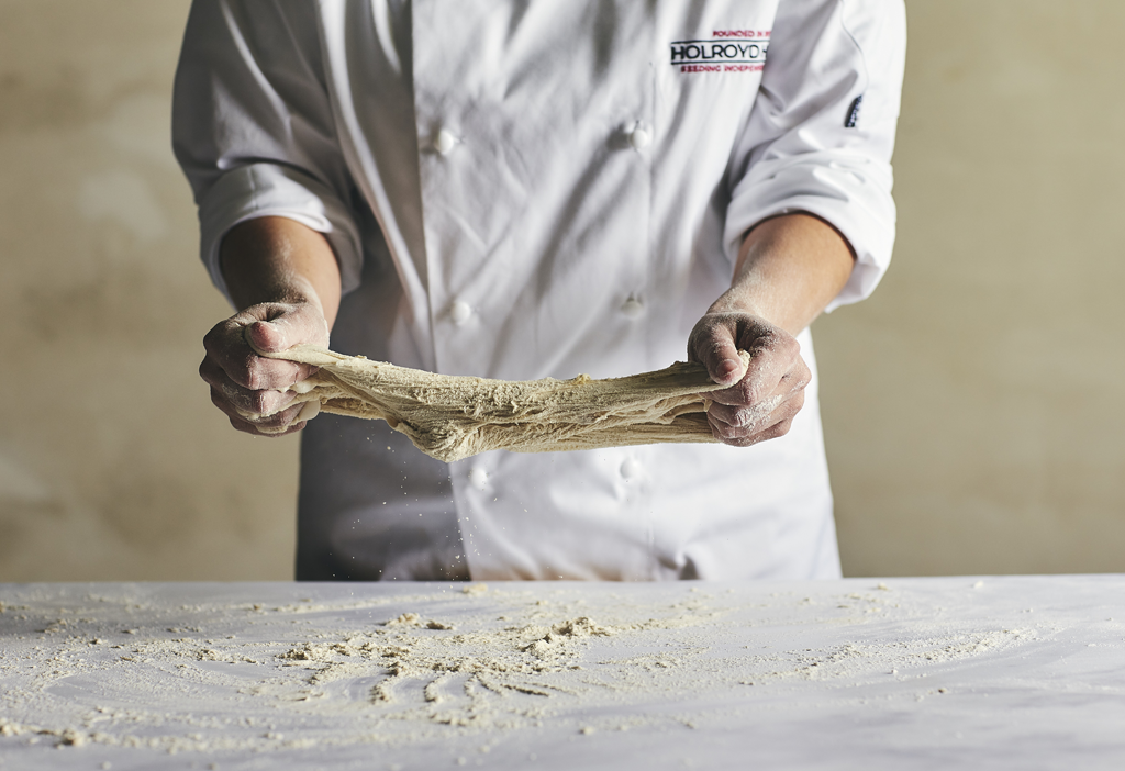 An image of chefs hands stretching bread dough at a table covered in flour