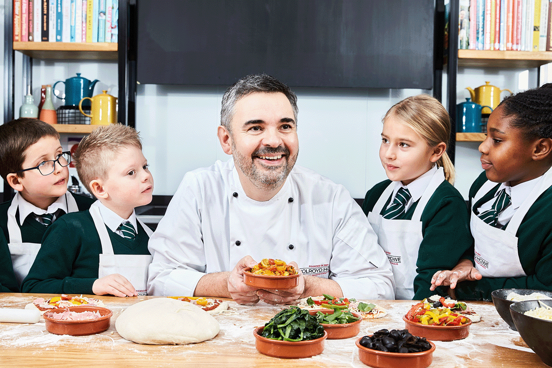 Bespoke catering services. An image of a chef around a table hosting a food demonstration to four pupils