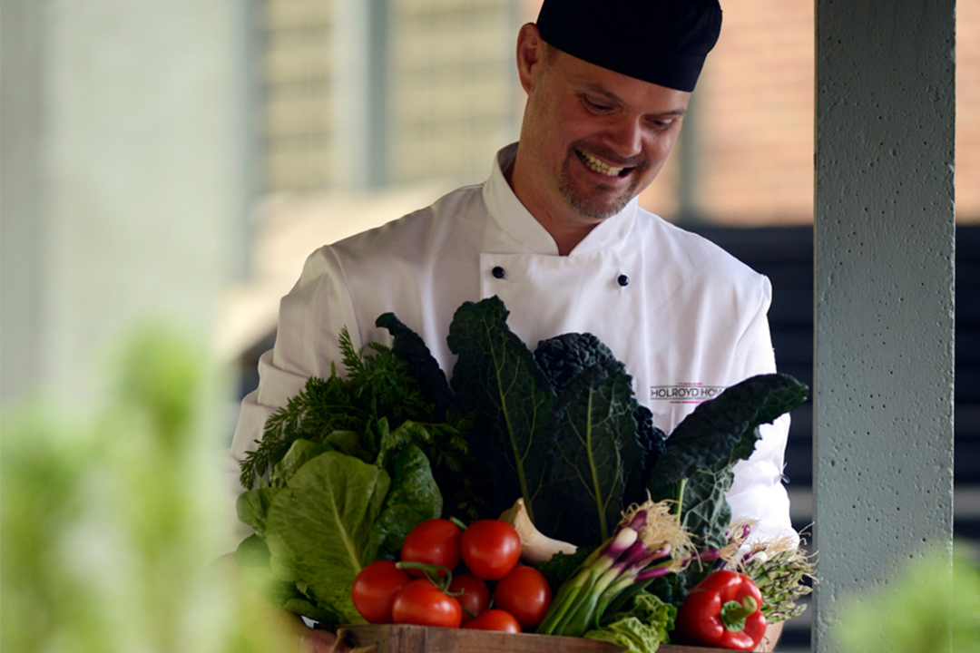 School dining. Image of a happy chef carrying fresh seasonal produce