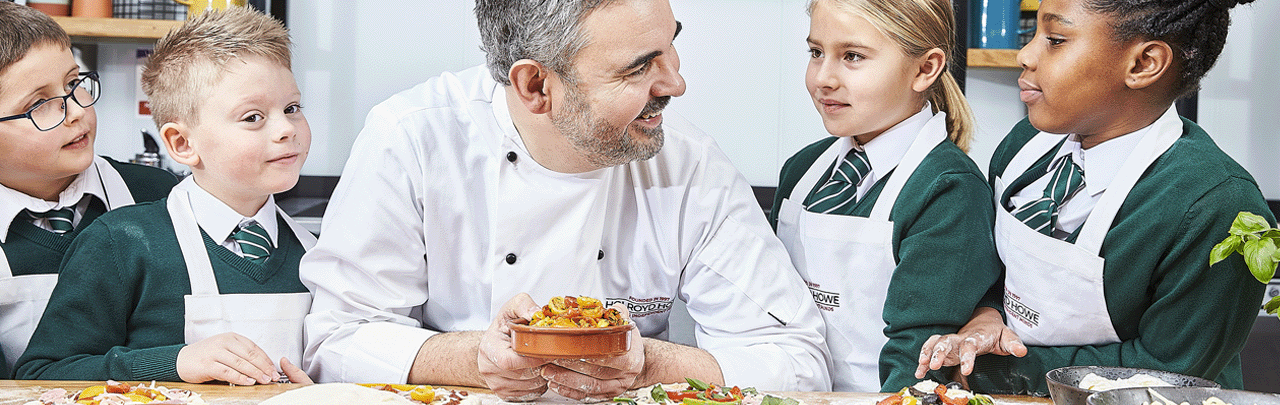 Our story. An image of a chef around a table hosting a food demonstration to four pupils